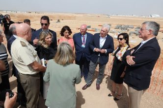 La ministra de Defensa y acompañantes reciben información sobre el Centro Integral de Entrenamiento y Movilidad Aérea del Ejército del Aire y del Espacio frente a las obras del mismo en el aeropuerto de Teruel.